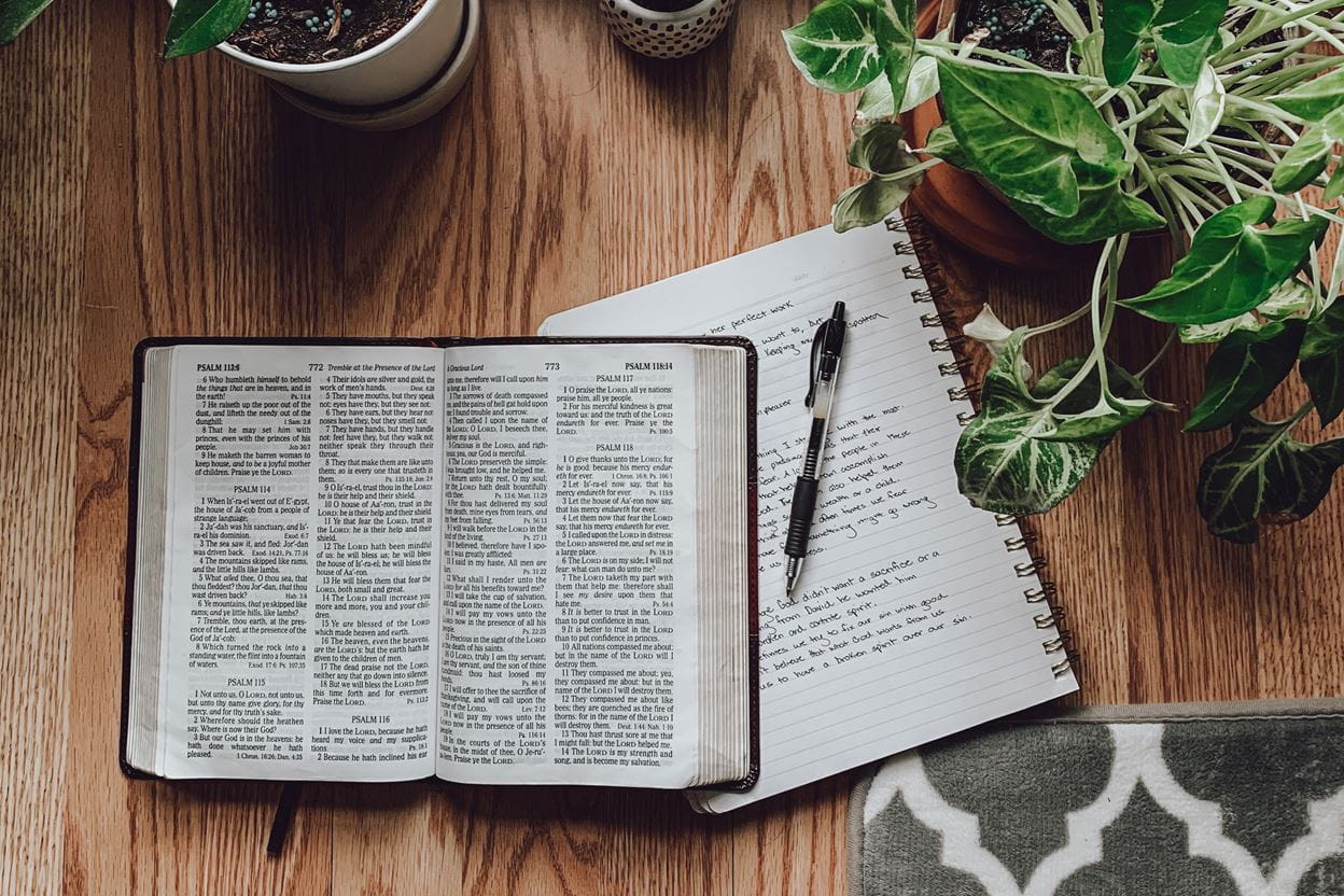 An open Bible and journal sitting on a table for ready for reading a daily devotional.