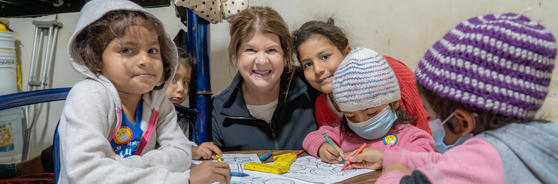 Image of Ginger Stache surrounded by a group of children smiling at a camera