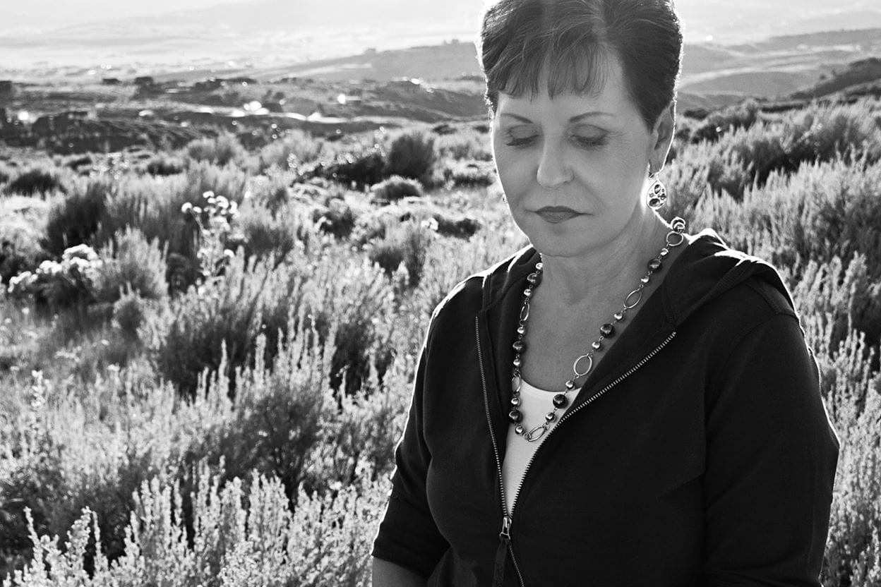 A black and white image of Joyce Meyer standing in a sunny field. A peaceful expression on her face. 