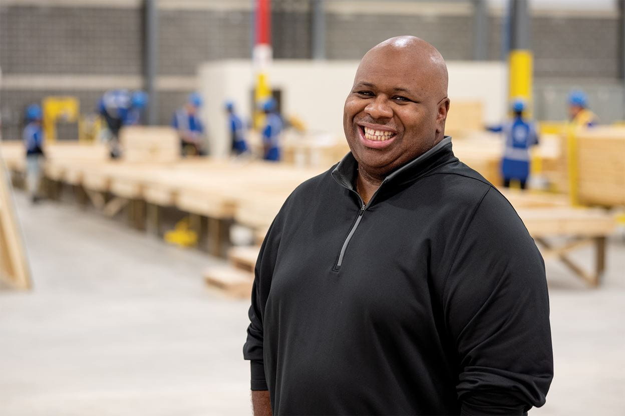 Amin Irving smiling in a warehouse with people working in the background