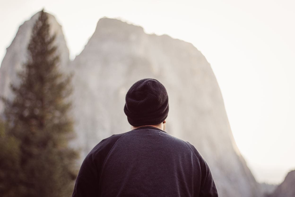 A man standing, staring at a tall mountain in front of him.
