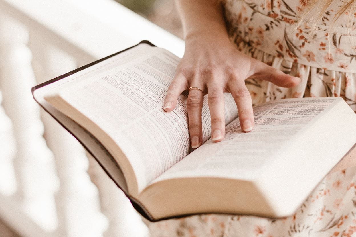 A woman holding a Bible open reading her daily devotional.