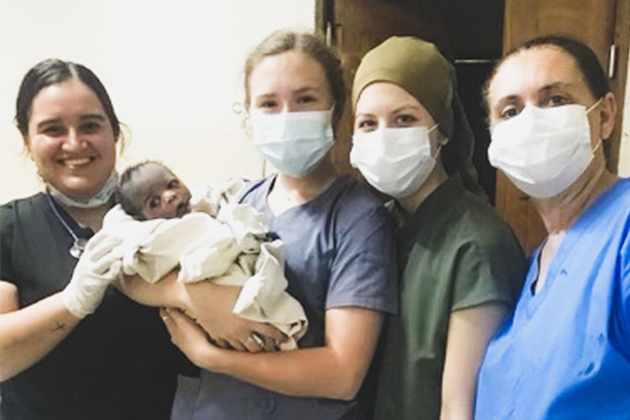 A team of nurses and doctors smiling and holding a baby named Hope.